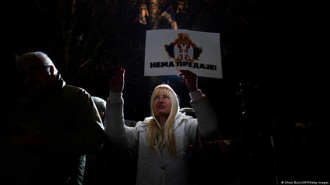 Woman holding poster showing Serbian flag superimposed over Kosovo and slogan