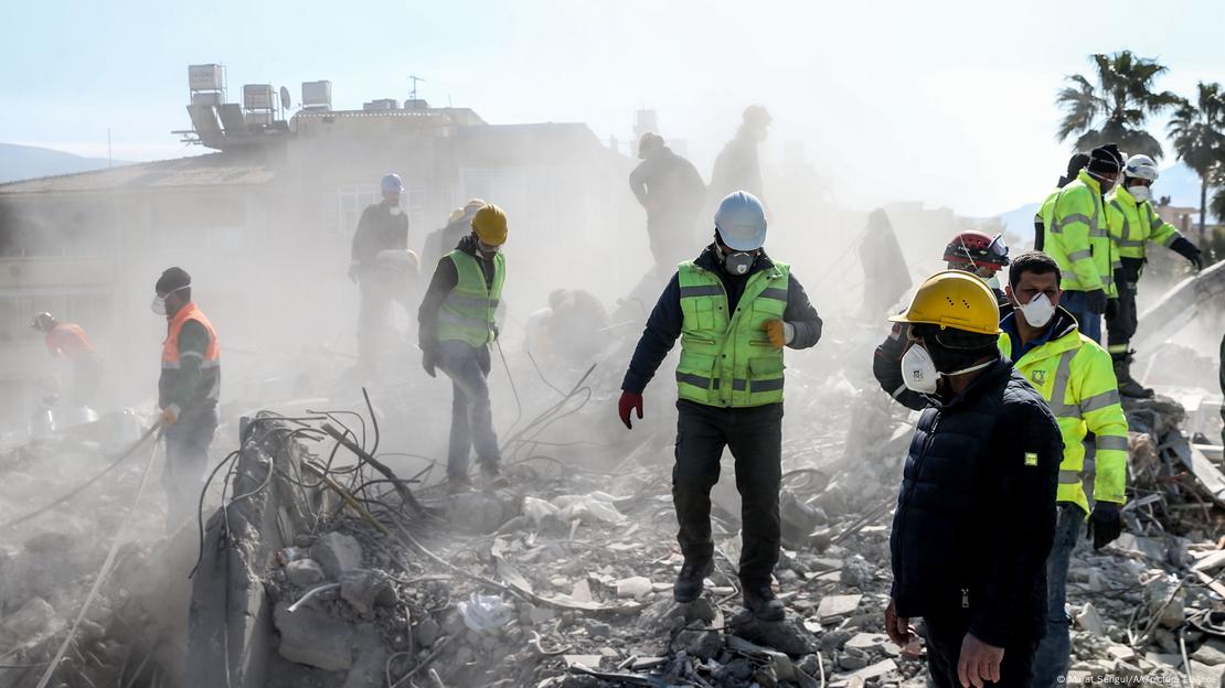 Homens caminham em meio a escombros e poeria em Hatay na Turquia 