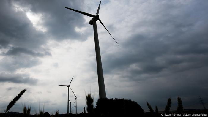 Windräder aus der Froschperspektive betrachtet vor dem Hintergrund eines dunklen, stark bewölkten Himmels.