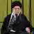 Der iranische Religionsführer Ajatollah Ali Chamenei sitzt vor einem grünen Vorhang hinter zwei Mikrofonen