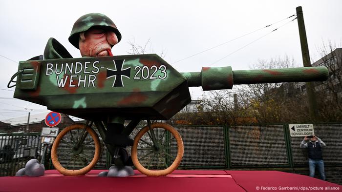 Karneval in Düsseldorf: Das Bild zeigt einen Bundeswehrsoldaten auf einem Fahrrad, der eine Panzerattrappe mit sich führt