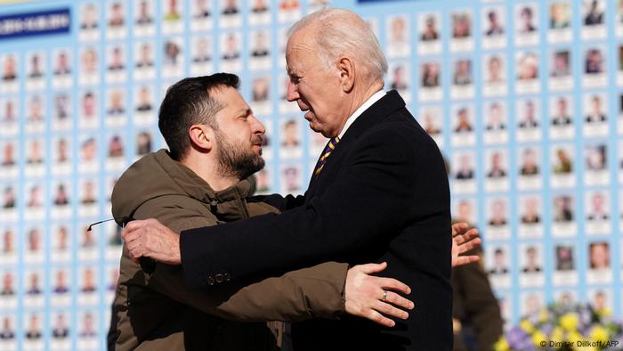 US-Präsident Biden umarmt den ukrainischen Präsidenten Selenskyj vor einer Fotowand am Mahnmal für gefallene ukrainische Soldatinnen und Soldaten in Kiew