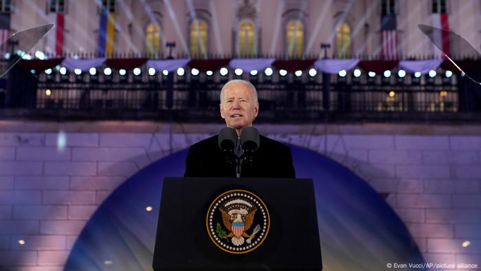 Biden am Rednerpult mit Wappen, dahinter eine beleuchtete Schlosskulisse