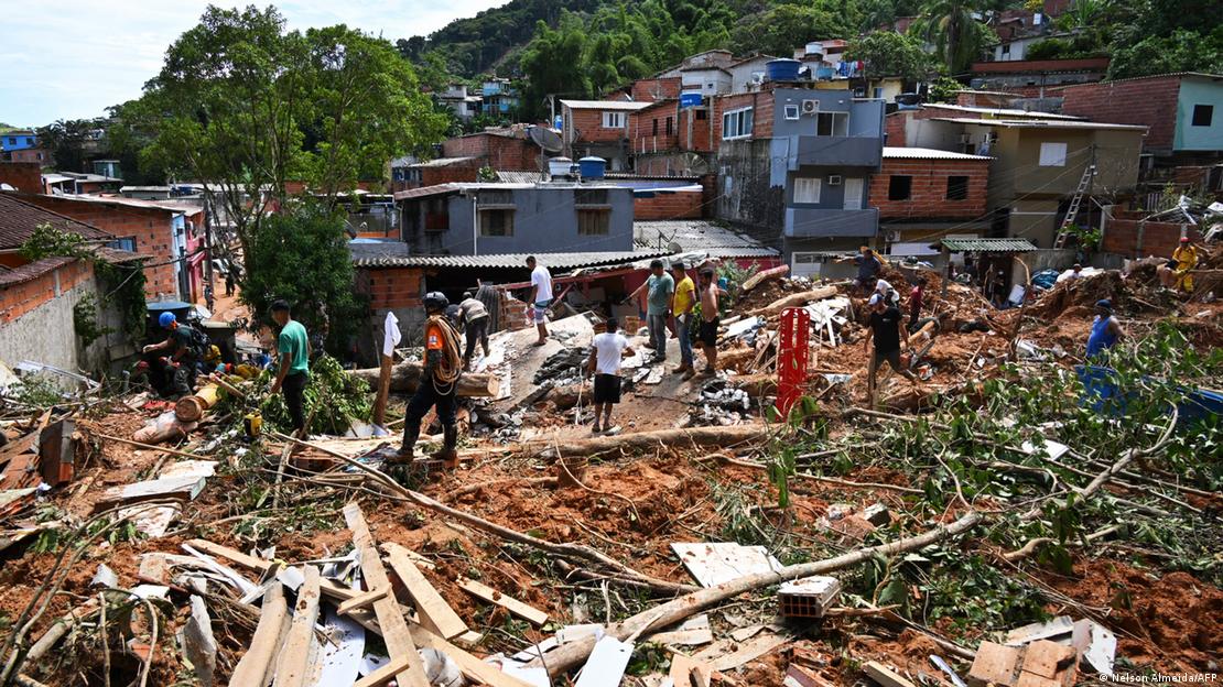 Pessoas em meio a casas destruídas e árvores derrubadas em encosta de São Sebastião, litoral de São Paulo