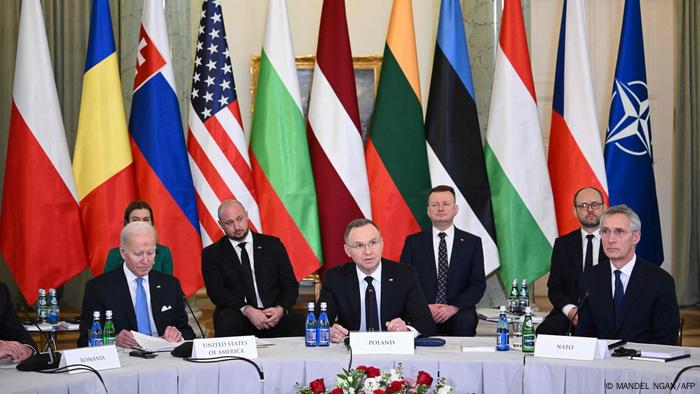 Am Tisch sitzen, von links: US-Präsident Biden, der polnische Präsident Andrzej Duda und NATO-Chef Jens Stoltenberg, im Hintergrund sitzen Mitarbeiter der Delegationen vor den Fahnen der Bukarest 9