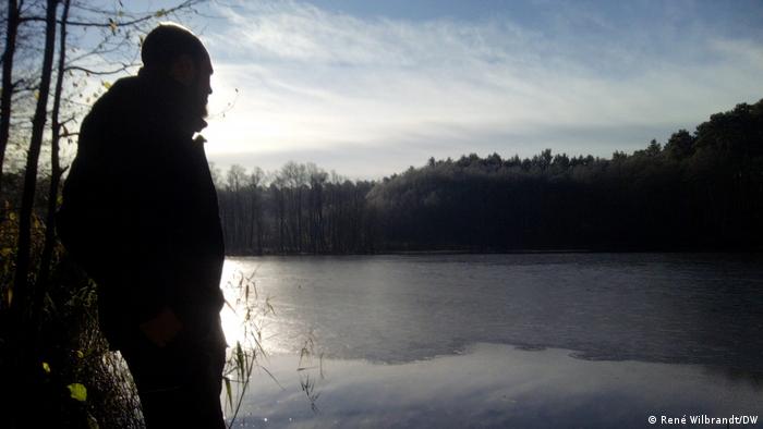 Ein Mann steht im Morgenlicht an einem See im Winter