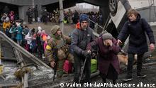 ARCHIV - 05.03.2022, Ukraine, Irpin: Eine ältere Dame wird bei der Überquerung des Flusses Irpin unter einer zerstörten Brücke unterstützt, während Zivilisten aus der Stadt fliehen. Am 24. Februar 2023 jährt sich der Beginn des russischen Angriffskrieges gegen die Ukraine. (zu dpa «Was von einem Jahr Krieg besonders in Erinnerung bleibt») Foto: Vadim Ghirda/AP/dpa +++ dpa-Bildfunk +++