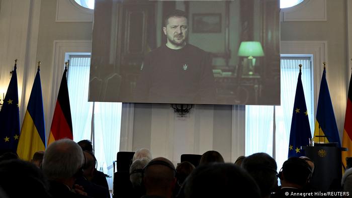 Der ukrainische Präsident Wolodymyr Selenskyj spricht während einer Gedenkveranstaltung zum Jahrestag des russischen Einmarsches in der Ukraine im Schloss Bellevue in Berlin per Videobotschaft zu den Anwesenden