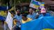 A group of people stand on the street waving Ukraine flags. A group of people stand on the street waving Ukraine flags.