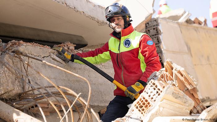 Notfallmediziner Daniel Lankers von ISAR Germany steht zwischen Trümmern im türkischen Erdbebengebiet in Krikihan, Hatay