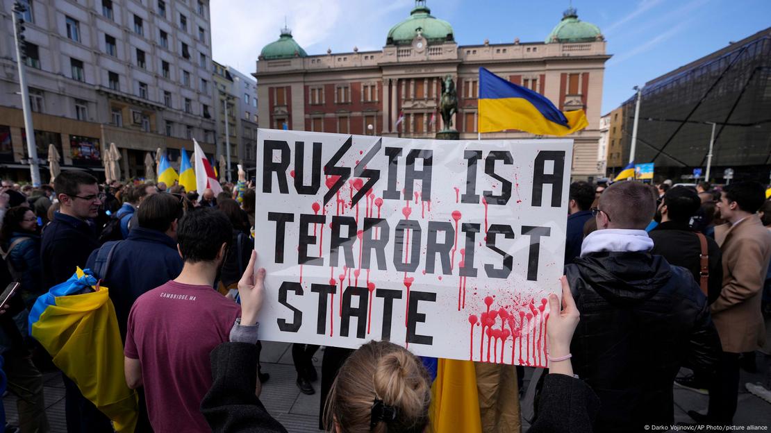 A woman, part of a large crowd, holds a banner reading 