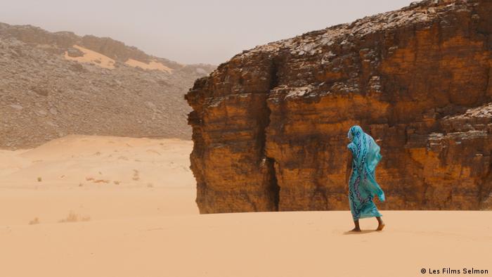 Eine Frau im blauen Gewand läuft durch die Wüste 