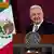 López Obrador sonríe en el atril con la bandera mexicana detrás.