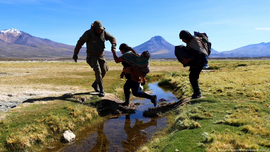 Un policía chileno ayuda a unas personas a atravesar un canal cerca de Colchane. Un policía chileno ayuda a unas personas a atravesar un canal cerca de Colchane.