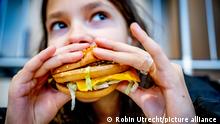 ROTTERDAM - A girl woman eats fries and a hamburger at a fast food restaurant. A fat tax is an excise duty levied on unhealthy and fatty foods Robin Utrecht