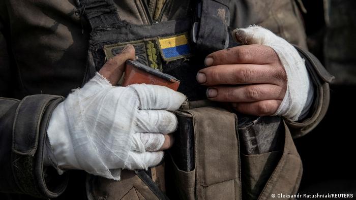 Primer plano de las manos vendadas del soldado sobre su pecho, en el que destaca también la bandera ucraniana.