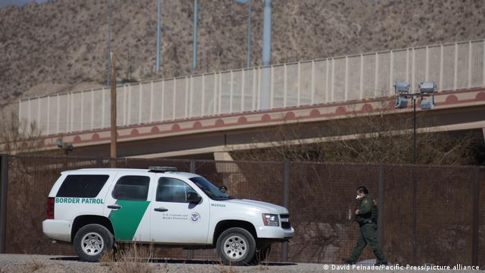 Ein Grenzbeamter in grünem Anzug und Schutzausrüstung geht auf einen Pick-up mit der Aufschrift Border Patrol zu.