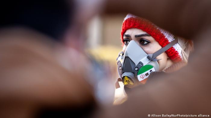 Eine Frau trögt eine Gasmaske, darauf die iranische Flagge