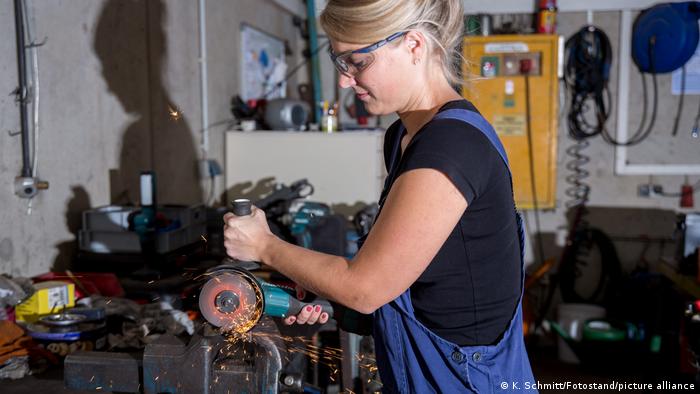 Eine Frau arbeitet im Beruf als Metallbauerin in einem Betrieb des Metallbau. Mit dem Winkelschleifer schneidet Sie ein Stück Metall auf Mass.
