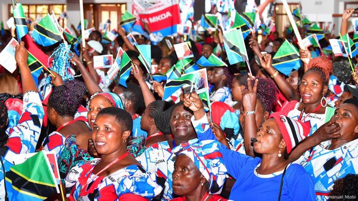 In weiß, blau, rot gekleidete Frauen stehen zusammen und schenken kleine Nationalflaggen von Tansania