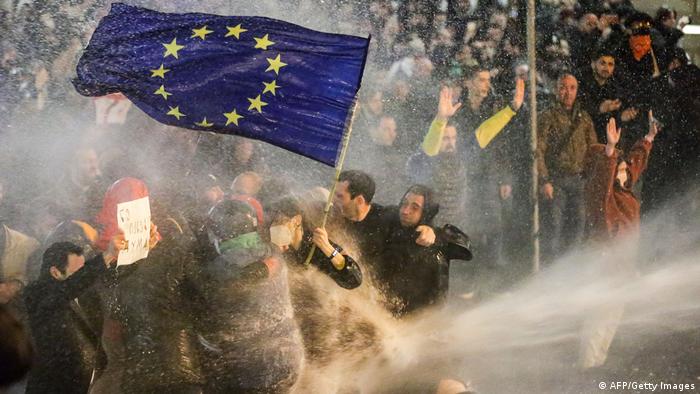 Eine Menschenmenge wird vom Wasserstrahl eines Wasserwerfers während der Proteste getroffen. Die Demonstranten halten ein europäische Flagge hoch.