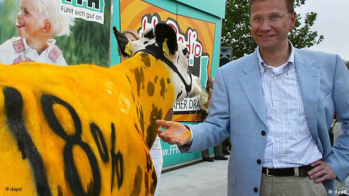 Guido Westerwelle pointing at a cow that has been painted yellow and has 18% written on its side