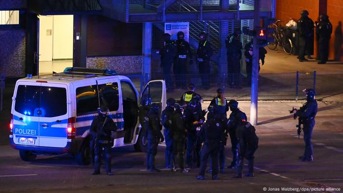 Polizisten mit Helmen und Schutzausrüstung und ein Polizei-Kleinbus stehen vor dem Gebäude, in dem die Schüsse fielen