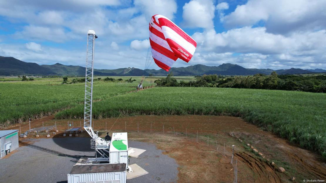 A huge red and white striped energy-creating kite hovers above the ground