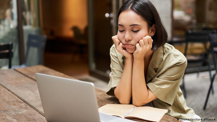 Eine junge Frau sitzt vor einem Laptop und hat ihren Kopf in die Hände gestützt. Ihr Gesicht drückt Unzufriedenheit aus.