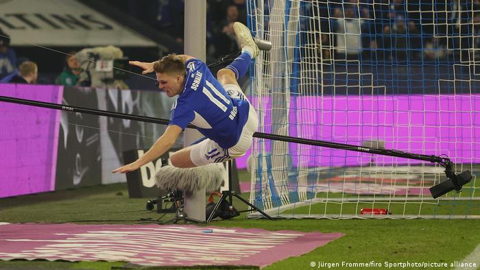 Schalkes Marius Bülter stürzt nach seinem Tor gegen Borussia Dortmund über die Halterung einer TV-Kamera