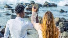 Moro and Lina seen from behind as they raise their joint hands to the sea