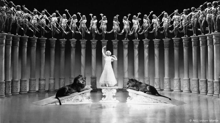 Escena de la película El gran Ziegfeld, en que una mujer alza los brazos. A sus costados hay dos leones.