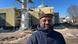 Malik stands in front of the construction site of the mosque wearing a hat and coat