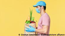 Profile view of delivery man holding food in paper bag wearing face mask and gloves as protection for COVID-19 Coronavirus precautions