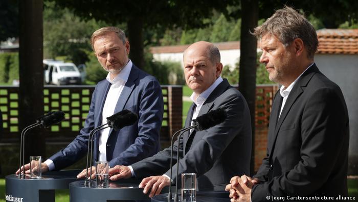 Christian Lindner, Olaf Scholz und Robert Habeck stehen bei der Kabinettsklausur in Meseberg vor Rednerpulten, die für eine Pressekonferenz vor dem Schloss aufgestellt wurden. Die drei Politiker haben ernste Mienen.