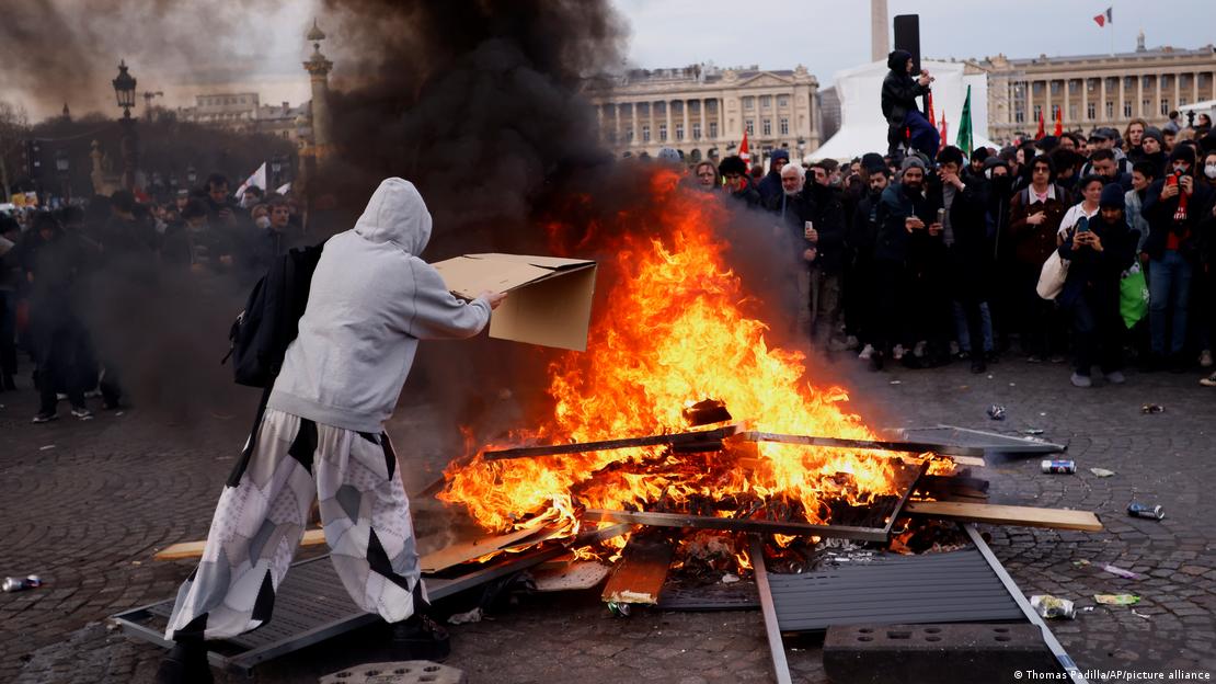En demonstrant kastar en kartong för att mata brinnande lastpallar under en demonstration på Concorde-torget nära nationalförsamlingen i Paris, torsdagen den 16 mars 2023.