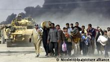 Menschen fliehen aus Basra im Jahr 2003 im Hintergrund schwarzer Rauch und Panzer