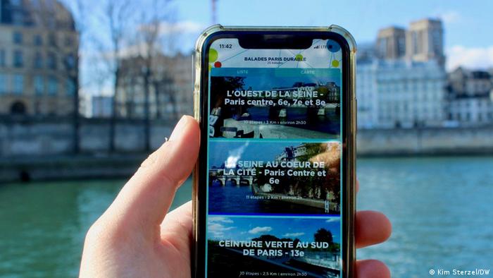 Eine Hand hält ein Handy, im Hintergrund die Seine in Paris