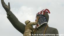 TOPSHOT - A US Marine covers the face of Iraqi President Saddam Hussein's statue with the US flag in Baghdad's al-Fardous square 09 April 2003. The flag was removed shrtly afterwards and replaced by the old Iraqi flag. US troops moved into the heart of the Iraqi capital meeting little resistance. AFP PHOTO/Ramzi HAIDAR (Photo by RAMZI HAIDAR / AFP) (Photo by RAMZI HAIDAR/AFP via Getty Images)