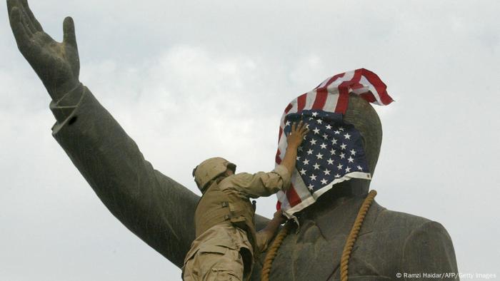 Ein US-Soldat umwickelt das Gesicht einer Statue von Saddam Hussein mit einer US-Flagge, ein Strick liegt um den Hals der Statue