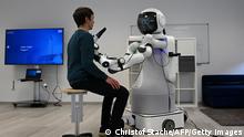 An employee sits in front of the robot Garmi in the laboratory of the Research Center Geriatronics of the Technical University Munich, in Garmisch-Partenkirchen, southern Germany, on March 6, 2023. - The white-coloured humanoid Garmi doesn't look much different from a typical robot -- it stands on a platform with wheels and is equipped with a black screen on which two blue circles acting as eyes are attached. (Photo by Christof STACHE / AFP) / TO GO WITH AFP STORY by Pauline CURTET (Photo by CHRISTOF STACHE/AFP via Getty Images)