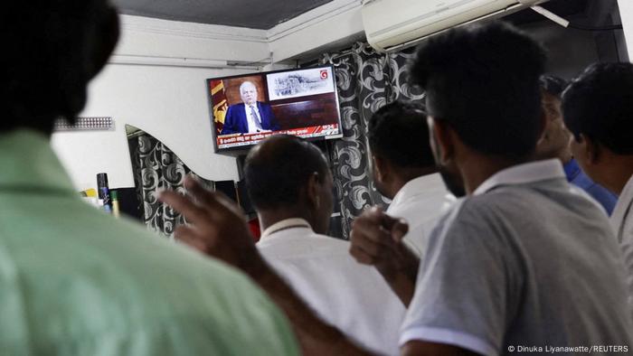 Habitantes de Sri Lanka miran en televisión al presidente Rani Wickremesinghe, quien anuncia el acuerdo con el FMI.