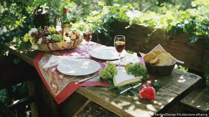 A table outside in a garden, set with bread, grapes and wineglasses.