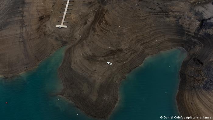 Ein Boot steht auf trockenem Boden, daneben Wasser