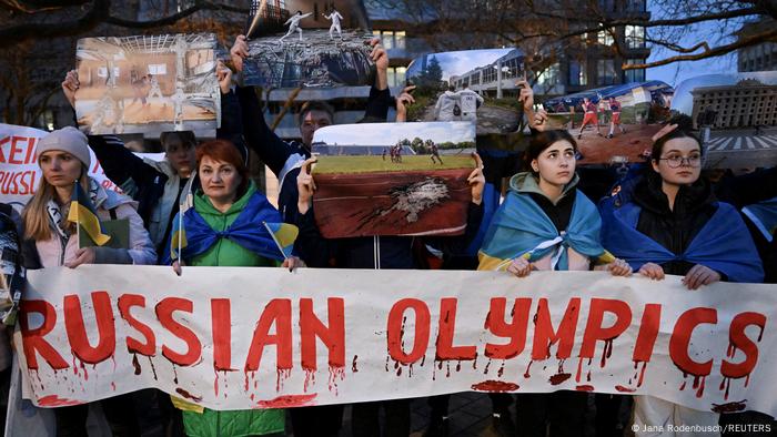 Ukrainische Demonstrantinnen tragen Banner mit der Aufschrift Russian Olympics, bestehend aus roten Buchstaben mit gemalten Blutstropfen