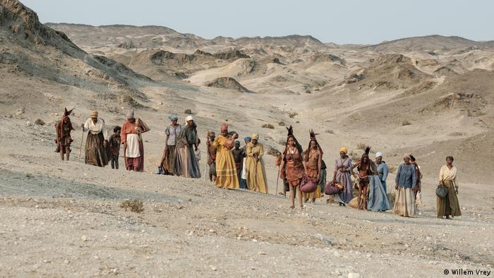 Wandernde Herero-Frauen mit Kindern in einer kargen Wüstenlandschaft