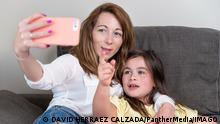 Happy mother with her daughter are making a video call to father or relatives in a sofa. Concept of technology, new generation, family, connection, parenthood.