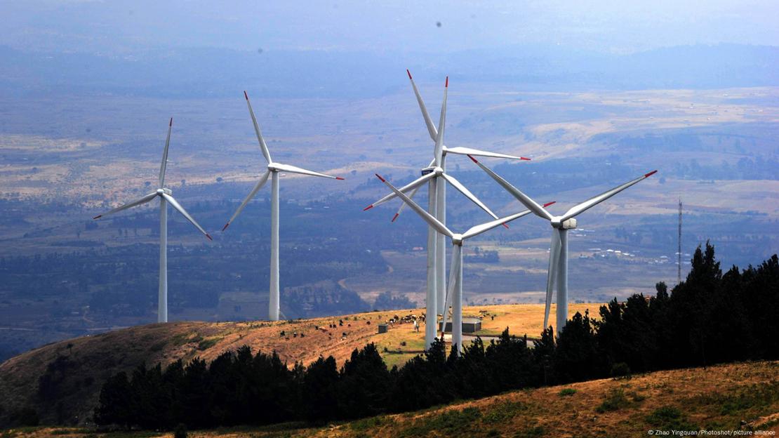 Wind turbines atop a hill with a vast landscape in the background.