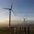 Wind turbines line a dirt road in Kenya as children look up at them from below