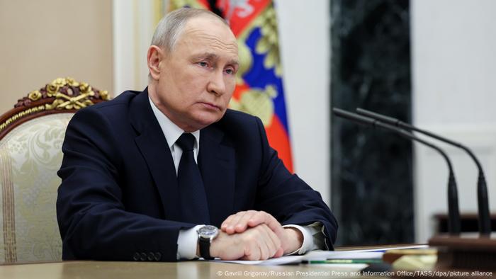 Präsident Russlands Wladimir Putin seit an einem Tisch vor Mikrofonen, März 2023
